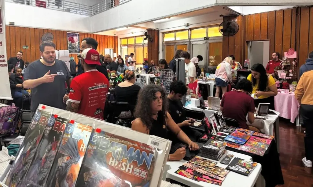 Evento de quadrinhos e colecionáveis com várias pessoas explorando e comprando produtos em um espaço bem iluminado.