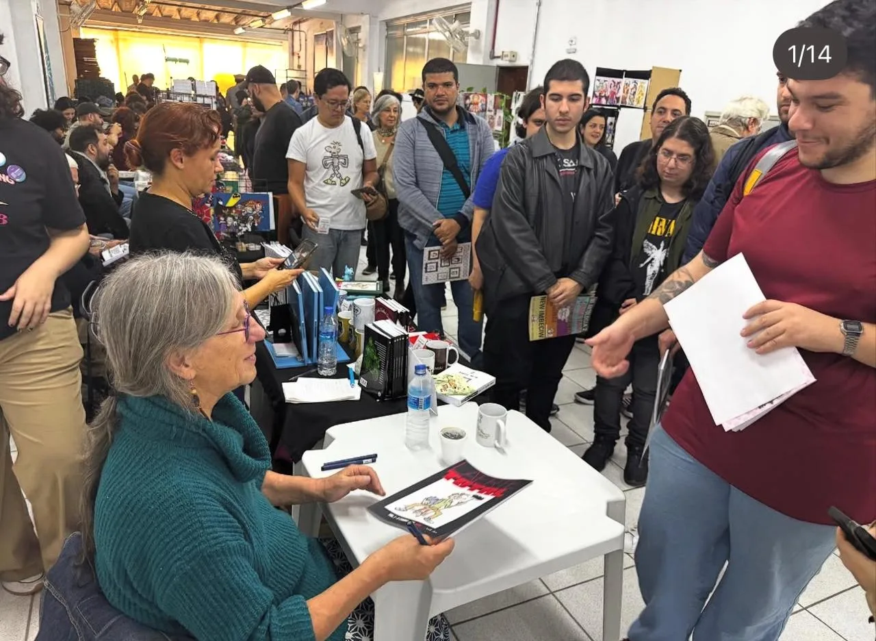 Laerte autografando exemplares para fãs em evento de quadrinhos, com muita fila e pessoas aguardando sua assinatura.