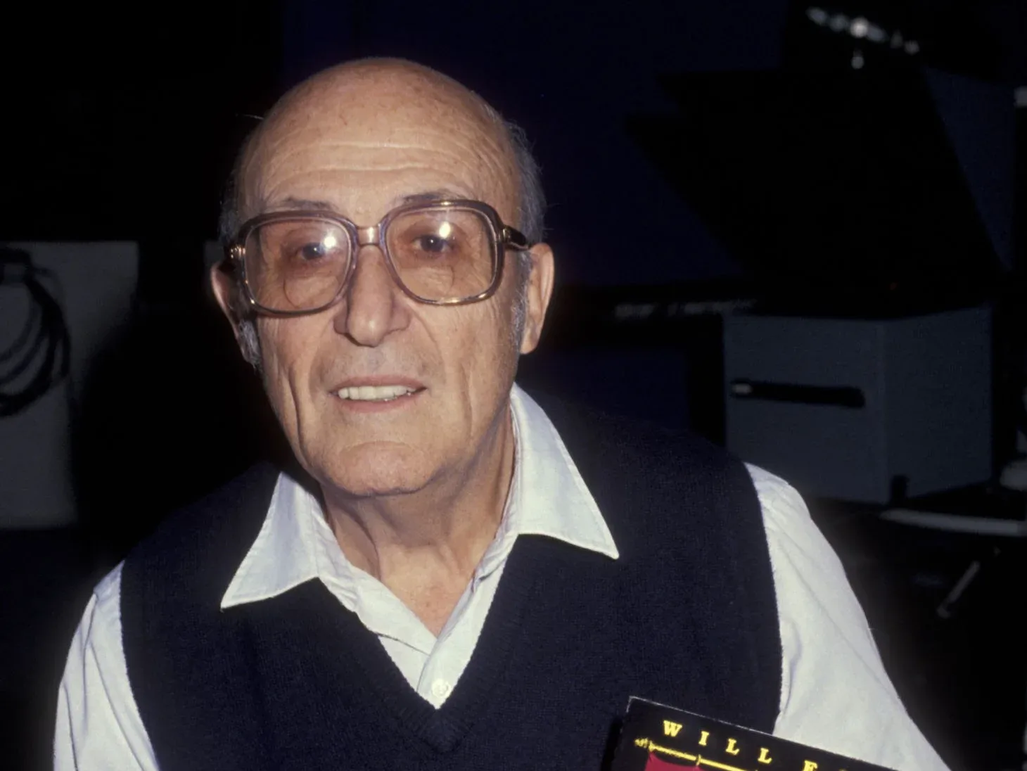 Foto de Will Eisner, um homem idoso vestindo camisa branca, suéter preto e óculos.